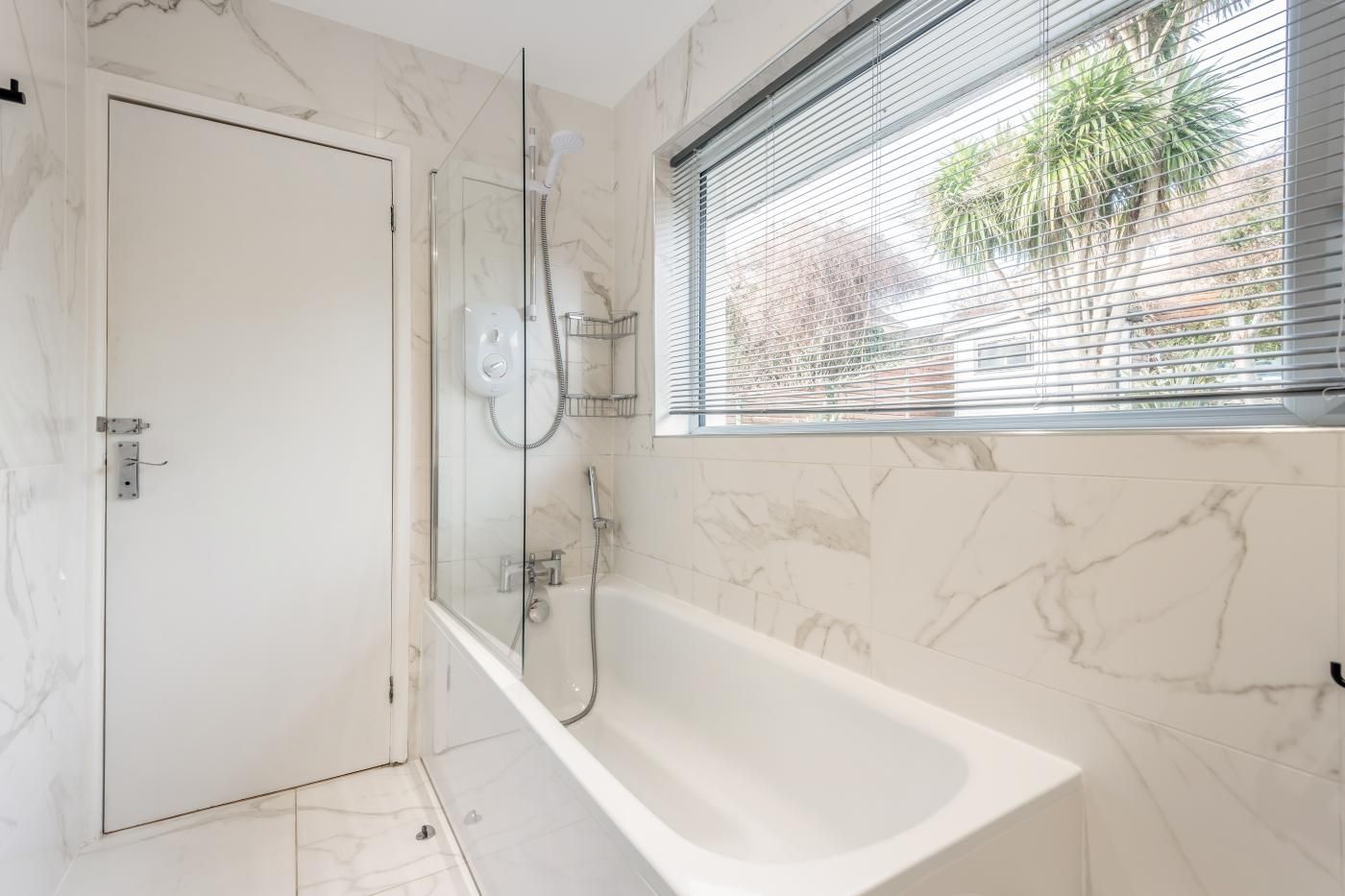 A bathroom with a glass-enclosed shower, a bathtub, and a window with blinds.
