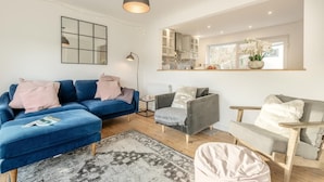 A modern living room with a blue sofa, grey armchair, and a small table. There is a mirror above the table, a hanging pendant light, and a patterned rug on the floor. - 2 Bed in Wareham (oc-79228) (West Lulworth)