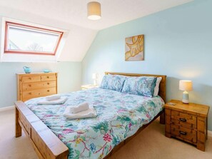 Ein Schlafzimmer mit einem Bett, einem Holzschrank, einem Nachttisch, einer Lampe, einem Fenster und einer Deckenleuchte.