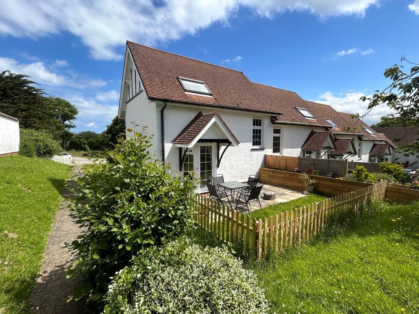 Une maison à deux étages avec un toit en pente, une fenêtre de grenier visible et une cour arrière clôturée, aménagée avec une table et des chaises de patio.