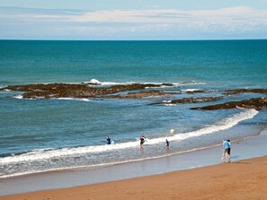 A beach with clear water, rocky outcrops, and people engaging in water activities. - 2 Bed in Cardigan (oc-79160) (Blaenannerch)