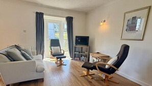Ein Wohnzimmer mit einer Couch, zwei Sesseln, einer TV-Bank und einem Gemälde an der Wand.