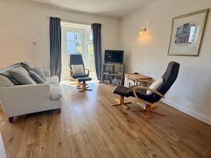 Ein Wohnzimmer mit einer Couch, zwei Sesseln, einer TV-Bank und einem Gemälde an der Wand.