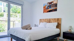 A bedroom with a bed, a wooden headboard, a nightstand, a lamp, and a window with a view of greenery. - 2B Near Vaugrenier, AC, terrace, sea view, swimming pool, parking- BENAKEY (Villeneuve-Loubet)
