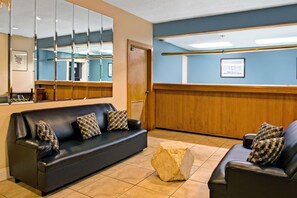 Un hall d’hôtel avec un canapé en cuir noir, un banc en bois et un grand miroir qui reflète la pièce.