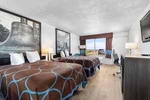 Habitación de hotel con dos camas, un ventanal grande, televisor y escritorio.
