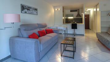 A modern living room with a grey sofa, red cushions, a small table, and a kitchen area in the background.