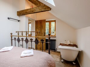 A bedroom with a bed, a wooden ceiling beam, a window, a radiator, and a white bathtub. - 1 Bed in Glastonbury (oc-79123) (Glastonbury)