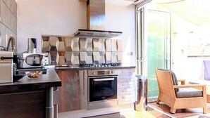 Una cucina con elettrodomestici in acciaio inossidabile, forno integrato e zona pranzo con sedia in vimini.