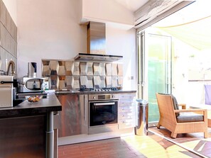 A kitchen with stainless steel appliances, a built-in oven, and a dining area with a wicker chair. - Downtown apartment with beautiful terrace and air conditioning- BENAKEY (Cannes)