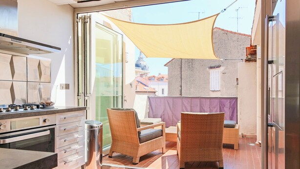Una cucina moderna con piano cottura a gas, forno e pensili in acciaio inossidabile. C'è un'area pranzo con mobili in vimini e un patio con tavolo e sedie.