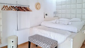 Una camera da letto moderna con un letto, una panca, un appendiabiti e un cestino.