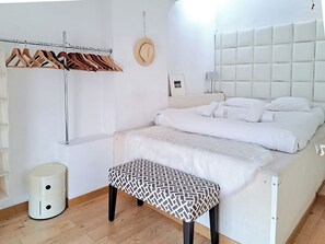 A modern bedroom with a bed, a bench, a coat rack, and a small trash bin. - Downtown apartment with beautiful terrace and air conditioning- BENAKEY (Cannes)