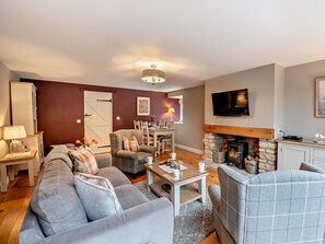 Ein Wohnzimmer mit Sofa, Sesseln, Kamin, Fernseher und Essbereich mit Tisch und Stühlen.