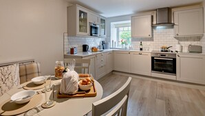 Ett modernt kök med vita skåp, en mikrovågsugn, en ugn och en matplats med ett bord dukat för två personer.