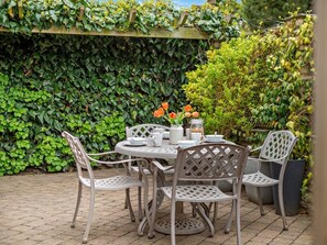 Eine Terrasse mit Tisch für vier Personen, umgeben von Stühlen und einer üppigen grünen Wand im Hintergrund.