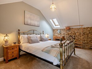 Ein Schlafzimmer mit einem Bett, Nachttischen, einer Lampe, einer Steinwand und einem Oberlicht.