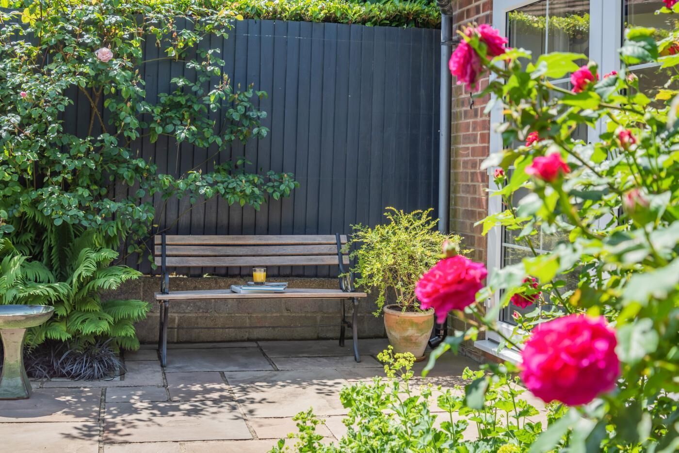 A patio with a wooden bench, a potted plant, and a metal birdbath.
