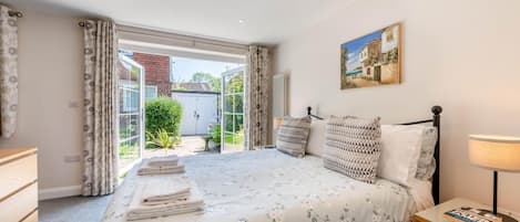 A bedroom with a bed, a bedside table with a lamp, a painting on the wall, and a view of the garden through the door.