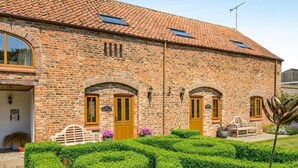 A brick building with a tiled roof, two arched doorways, and a small garden with hedges. - 2 Bed in Driffield (oc-79279) (Wold Newton)