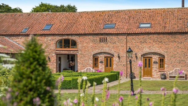 A brick building with a tiled roof, arched windows, and a well-maintained garden. - 2 Bed in Driffield (oc-79279) (Wold Newton)