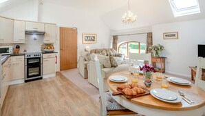 A modern kitchen with built-in appliances, a dining area with a round table set for breakfast, and a cozy living space with a sofa. - 2 Bed in Driffield (oc-79279) (Wold Newton)