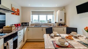 Una cocina moderna con un ventanal grande, un comedor listo para el desayuno y un televisor de pantalla plana montado en la pared.