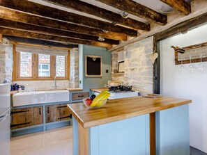 A rustic kitchen with exposed beams, a stone wall, a wooden countertop, and a window with a view. - 2 Bed in Glastonbury (oc-79122) (Glastonbury)