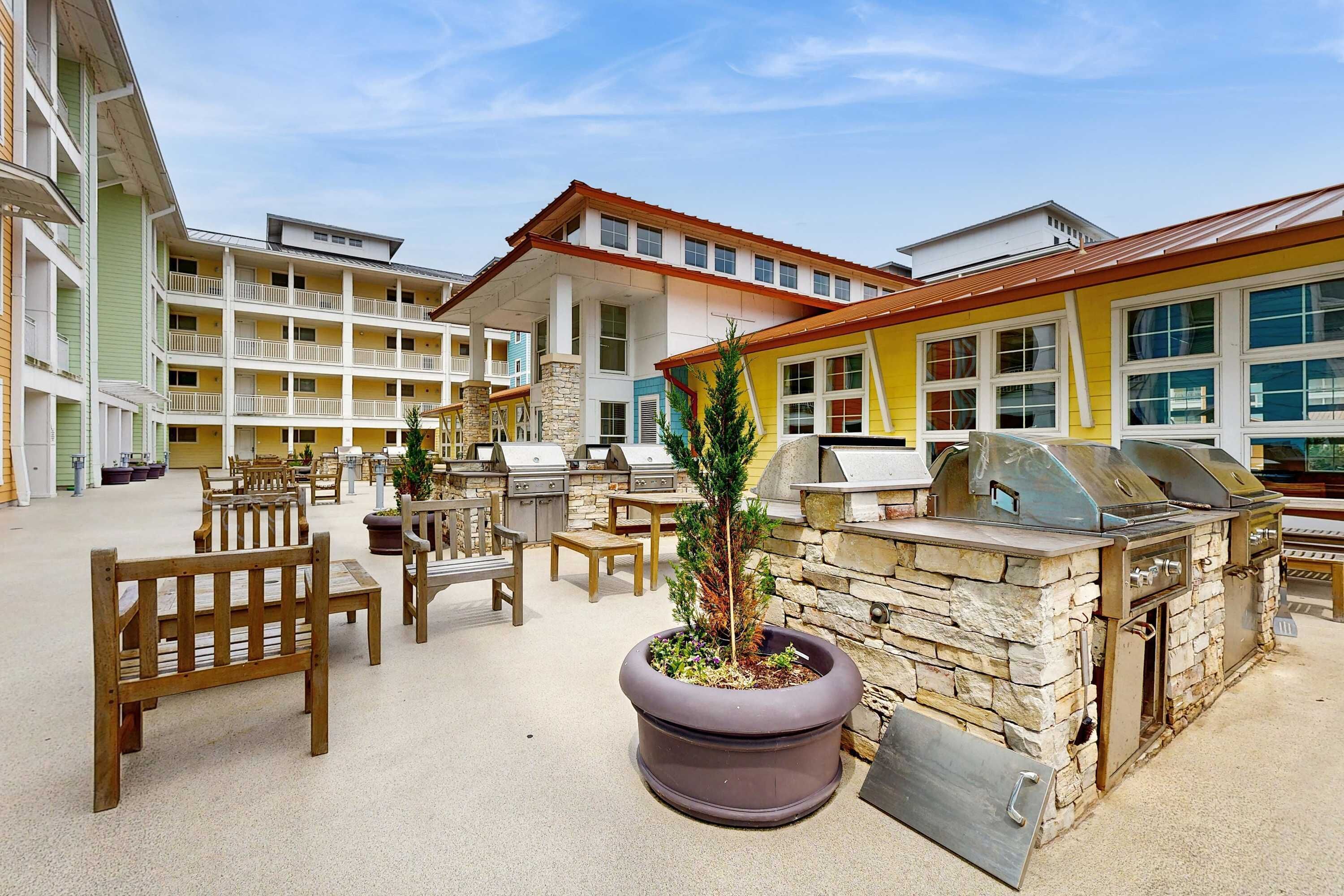 A courtyard with outdoor seating, a barbecue grill, and a stone planter with a small tree.