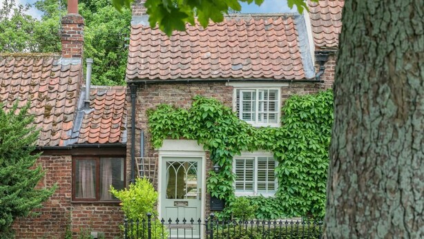 Una casa tradizionale in mattoni con tetto in tegole, pareti ricoperte d'edera e un ingresso con cancello.