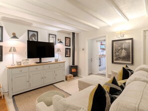 Ein Wohnzimmer mit Fernseher, heller Möbel, Kamin und gerahmten Bildern an der Wand.