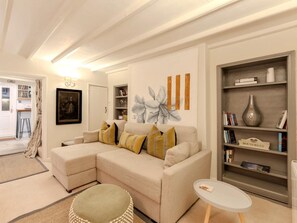 Ein Wohnzimmer mit einer Couch, einem kleinen runden Tisch, einem Bücherregal und einer Tür zu einem anderen Raum.