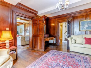 A spacious living room with wooden paneling, a large rug, a sofa, a lamp, and a painting on the wall. - 8 Bed in Rugeley (oc-79321) (Abbots Bromley)