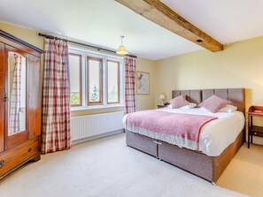 A bedroom with a bed, a nightstand, a lamp, a window with curtains, a radiator, and a wooden ceiling beam. - 8 Bed in Rugeley (oc-79321) (Abbots Bromley)