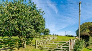 Paisaje rural con un portón de madera, árboles y cielo despejado.