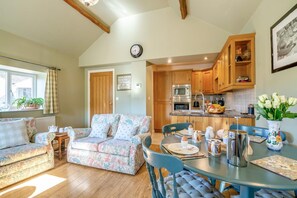 A cozy living room with a sofa and a dining table set for breakfast. A kitchen with wooden cabinets and appliances is visible in the background. - 2 Bed in Huby (oc-79166) (Weeton)