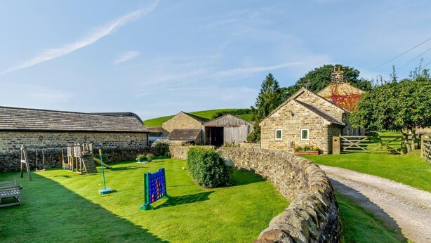 Un entorno rural con edificios de piedra, un patio con césped y un muro de piedra.