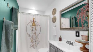 Um banheiro com cortina de chuveiro, vaso sanitário, pia, espelho e detalhes decorativos nas paredes.