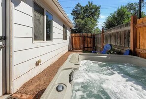 A hot tub adjacent to a white house with a wooden fence and a blue chair. - Evenstar Inn- Lord of the Rings & Private Hot Tub (Colorado Springs)
