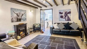 Een woonkamer met een open haard, een bank, een hond en kunstwerken aan de muur.