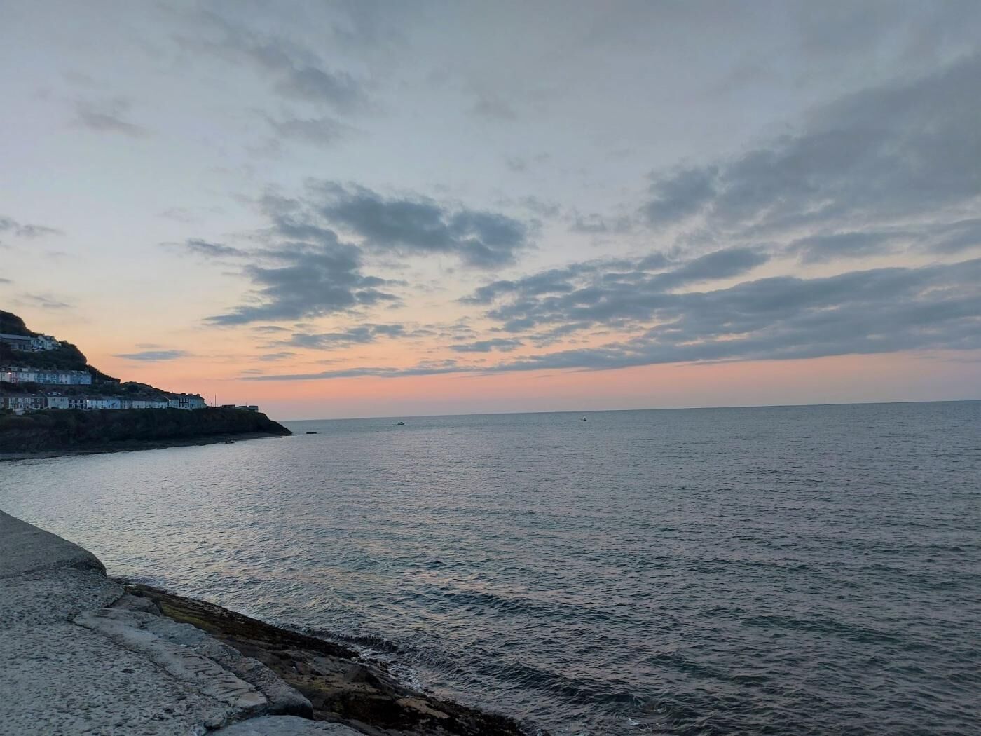 Un paysage côtier avec une mer calme, une côte rocheuse et des bâtiments situés sur une falaise.