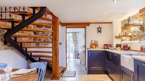 Eine Küche mit dunklen Schränken, einer Holztreppe und einem Essbereich mit Tisch und Stühlen.