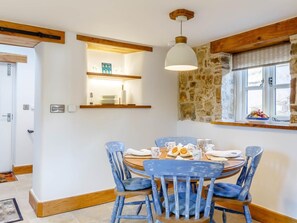 A dining area with a round table, blue chairs, a hanging light fixture, a stone wall, and a window with a view. - 2 Bed in Barnstaple (oc-79393) (Bishop's Tawton)