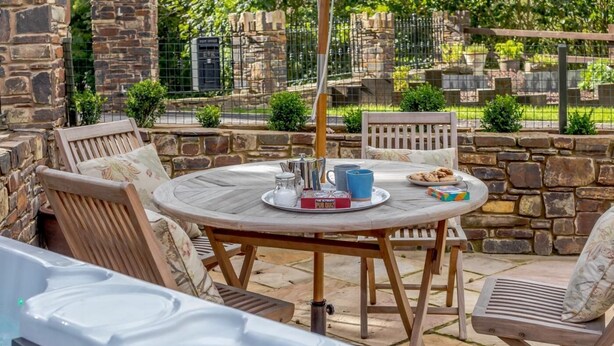 Eine Terrasse mit Whirlpool, Holzstühlen und einem Tisch mit Buch und Teekanne.