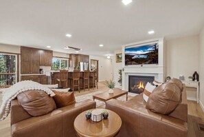 Una sala de estar moderna con chimenea, sofás de cuero, un comedor y una cocina al fondo.