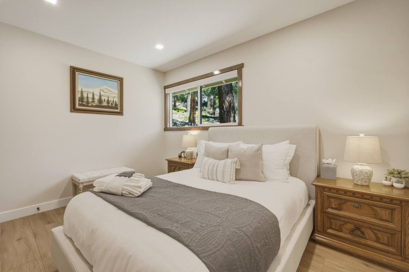 Une chambre avec un grand lit, deux tables de chevet, une fenêtre donnant sur des arbres, un tableau au mur et une lampe sur la table de chevet.