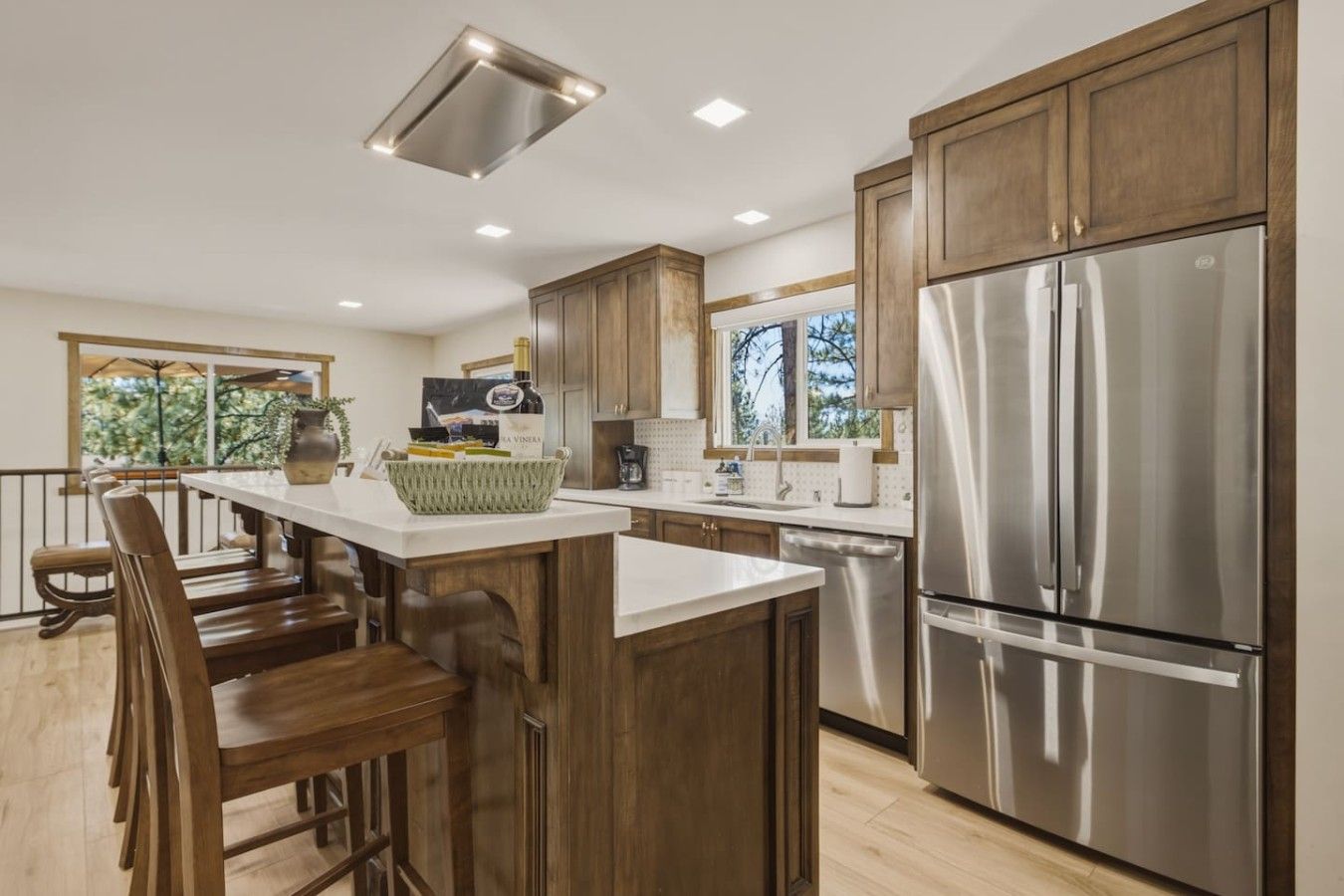 A modern kitchen with wooden cabinets, a stainless steel refrigerator, and a bar area with stools.