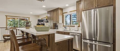 A modern kitchen with wooden cabinets, a stainless steel refrigerator, and a bar area with stools.