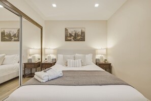 A hotel room with a large bed, two bedside tables with lamps, a mirror, and two paintings on the wall.