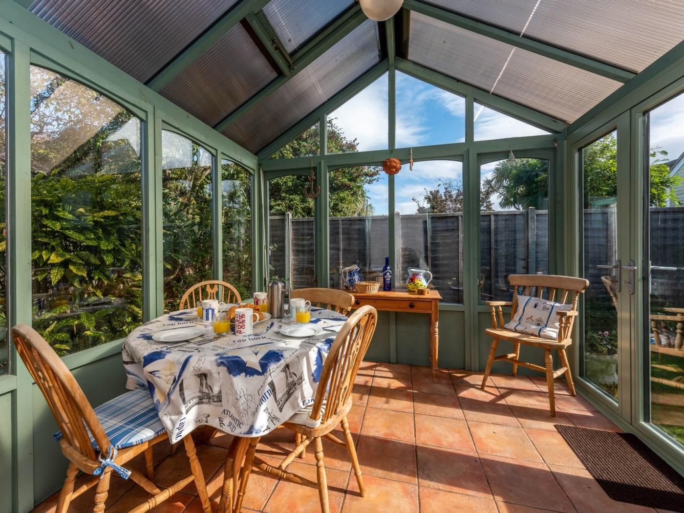 Un invernadero con una mesa lista para el desayuno, sillas y vistas al jardín.